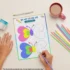 A person is drawing in a trace and color book on a table with a pen, sharpener, mug, and colorful pencils.