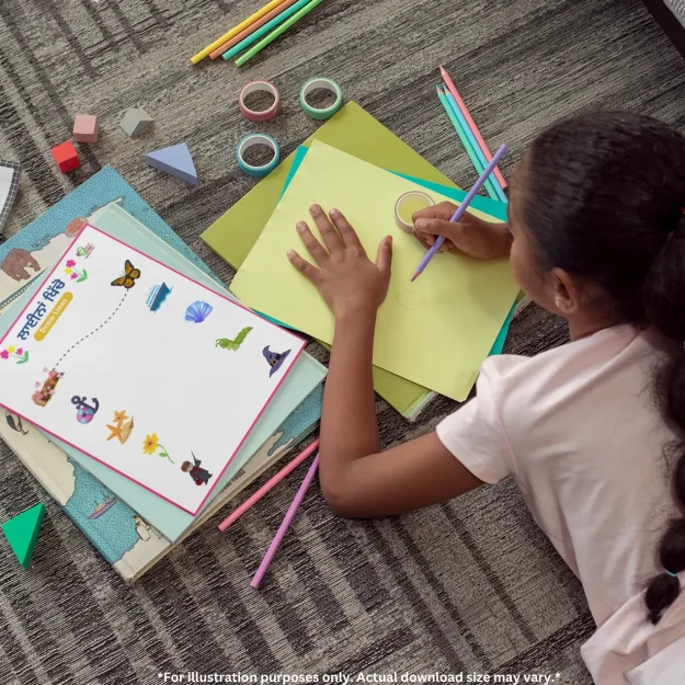 A preschool tracing worksheet is placed on other books near a kid drawing on chart paper, with many stationery items around it on the floor.